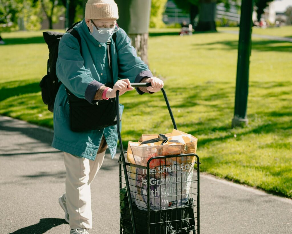 man in blue jacket and blue denim jeans holding shopping cart with basket of orange fruits