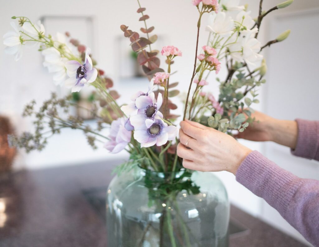 person holding white and purple flowers in clear glass vase