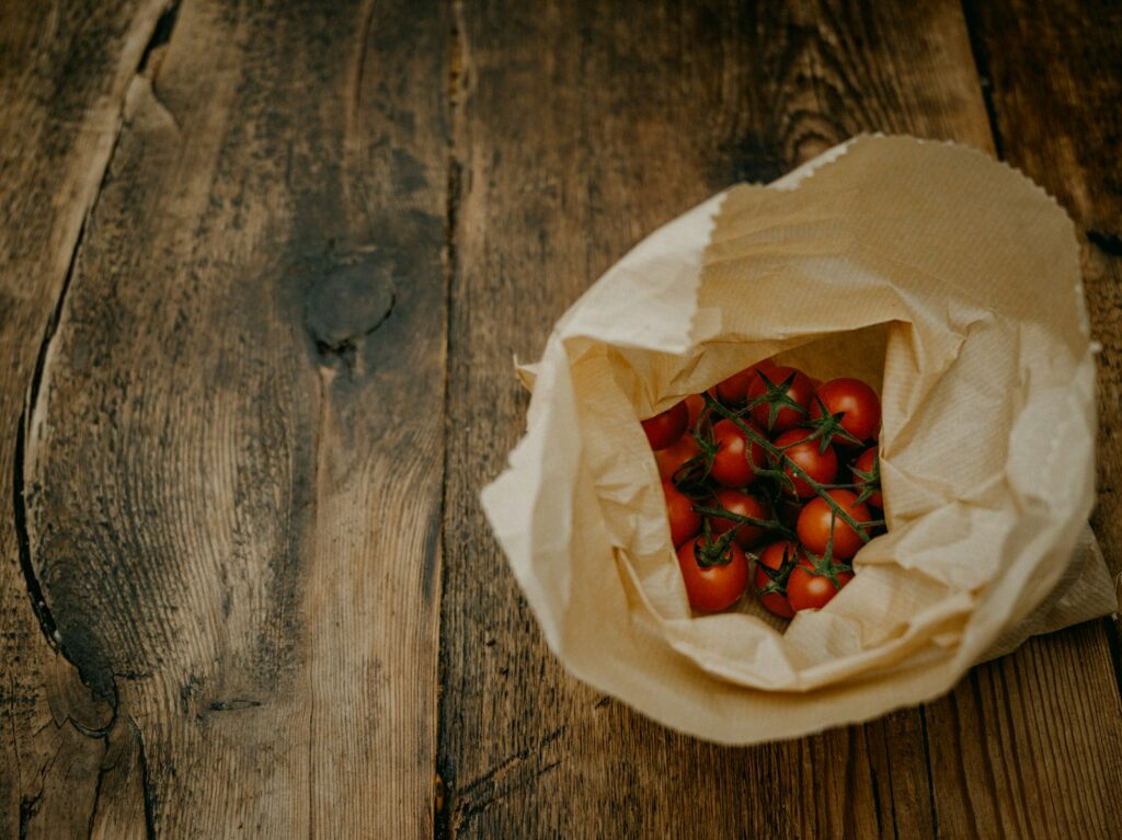 a paper bag filled with tomatoes on top of a wooden table