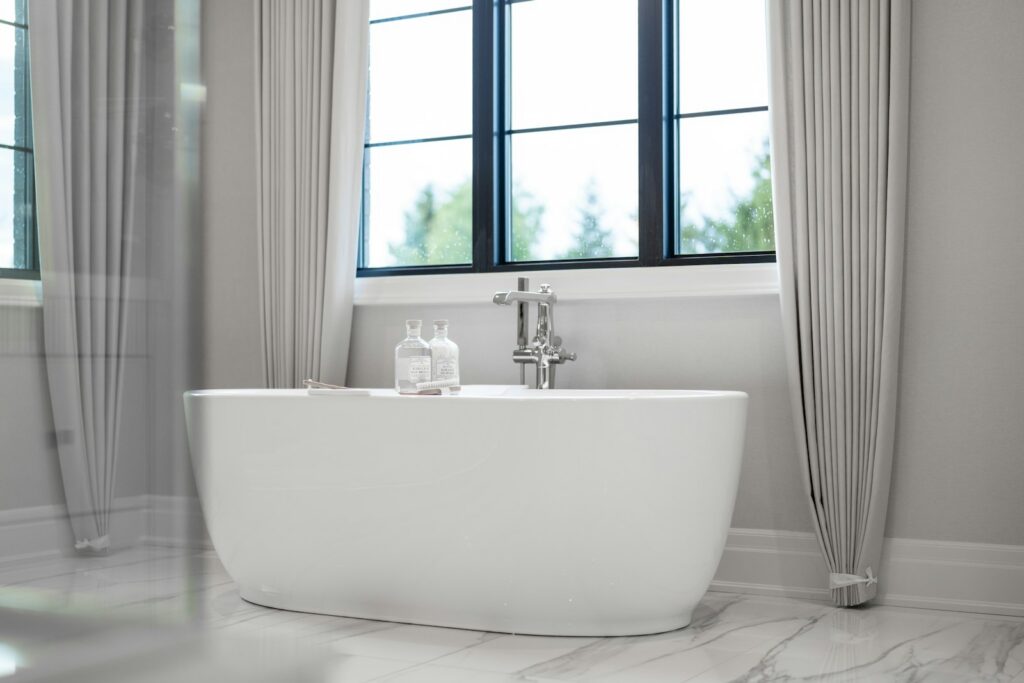 A modern white freestanding bathtub in a bright bathroom.