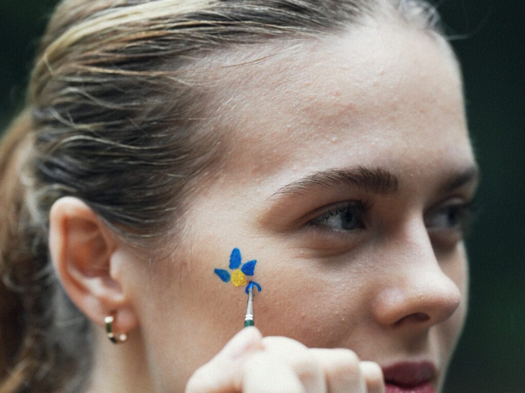 Artist applies blue and yellow flower face paint.