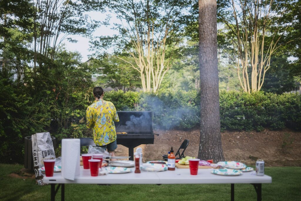 Person grilling outdoors with a table of food and drinks.