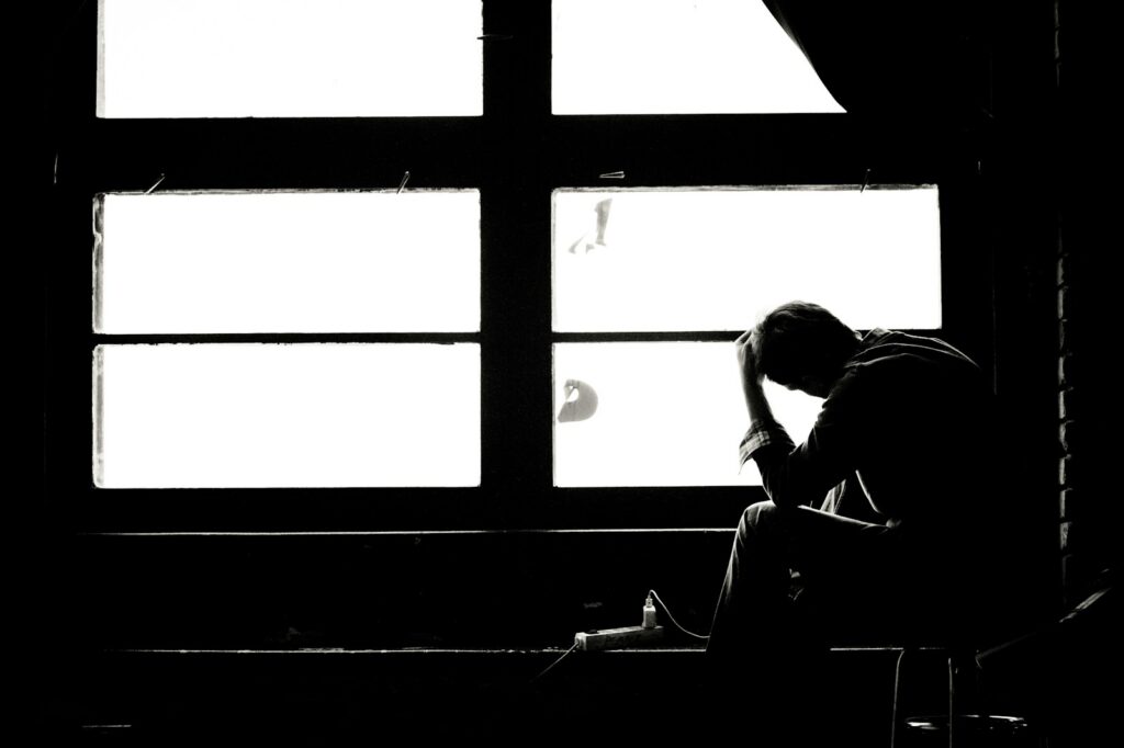 Person sitting alone by a window looking withdrawn