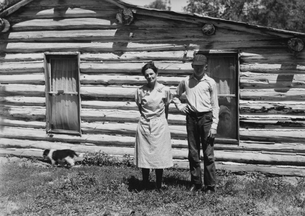 Couple standing in front of a rustic log cabin.