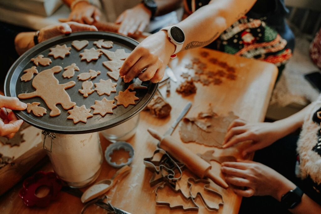 Hands arranging gingerbread cookies on a baking sheet.