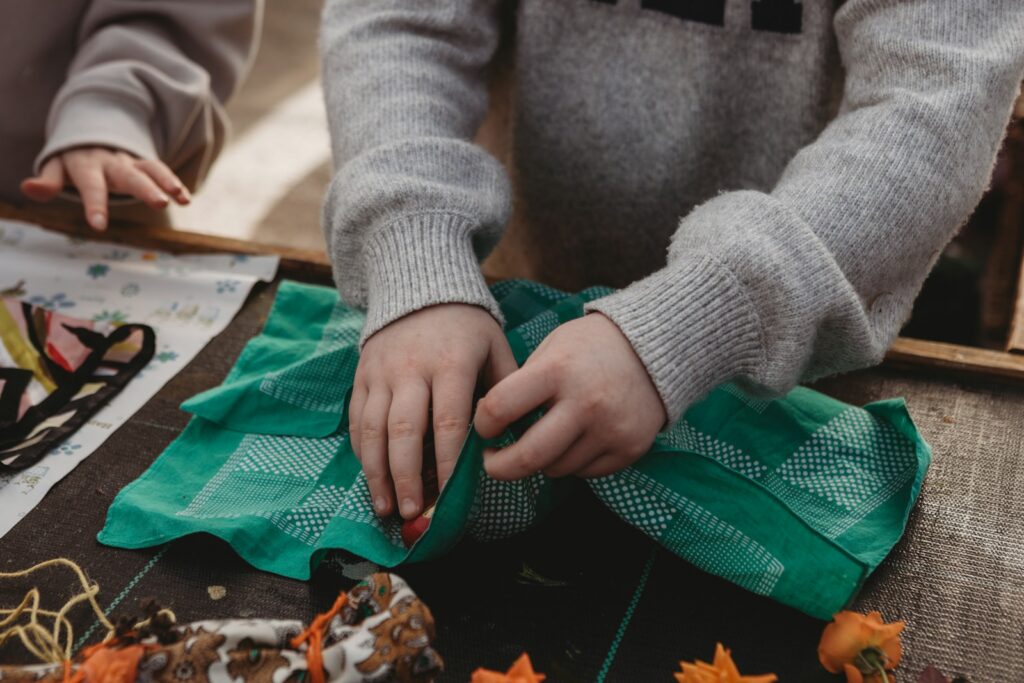 Child's hands folding a green cloth on a wooden table.