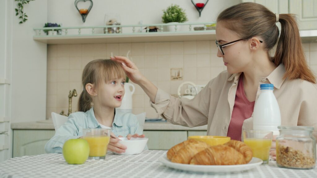 Mother touches daughter's hair during breakfast.