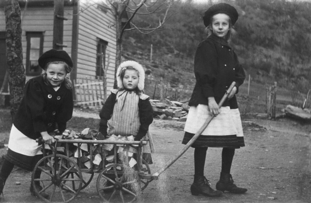 Three children with a toy wagon outdoors.