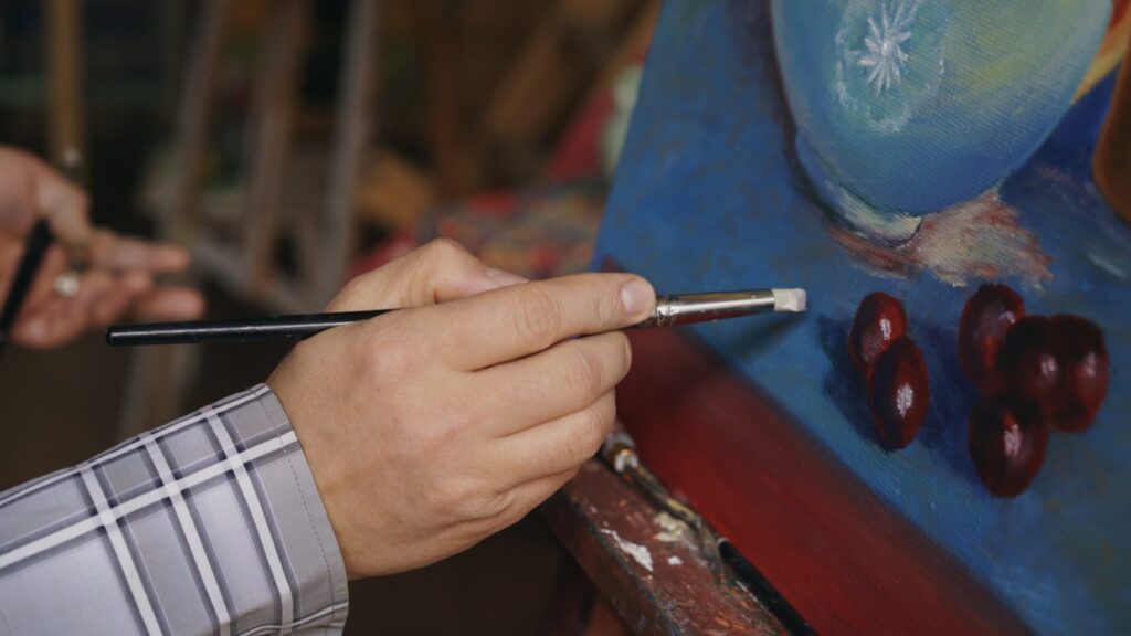 Artist painting a still life with cherries and blue vase.