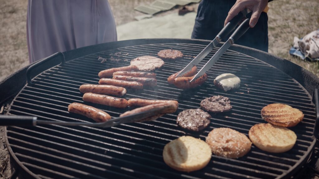 Hand turning sausages and burgers on an outdoor grill.