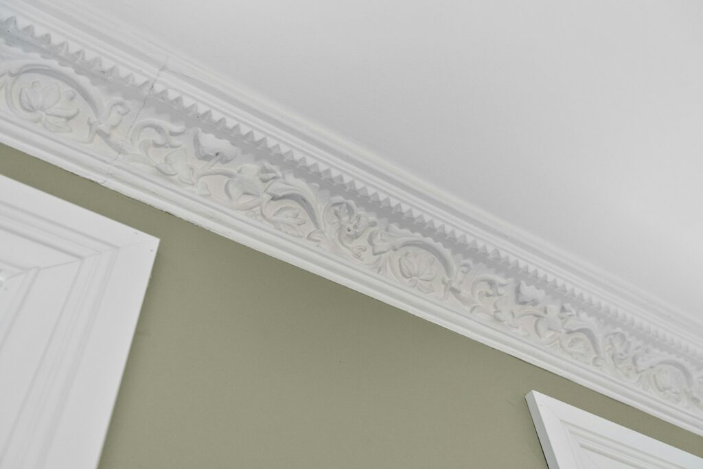 Ornate white decorative molding above a green interior wall