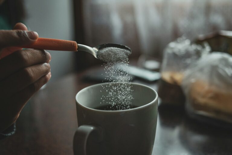person adding sugar to coffee cup